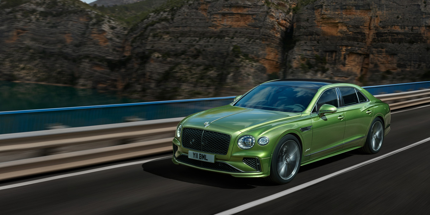 Bentley Paris Seine Bentley New Flying Spur Speed v8 hybrid sedan driving dynamically on a mountain road in Tourmaline Green paint