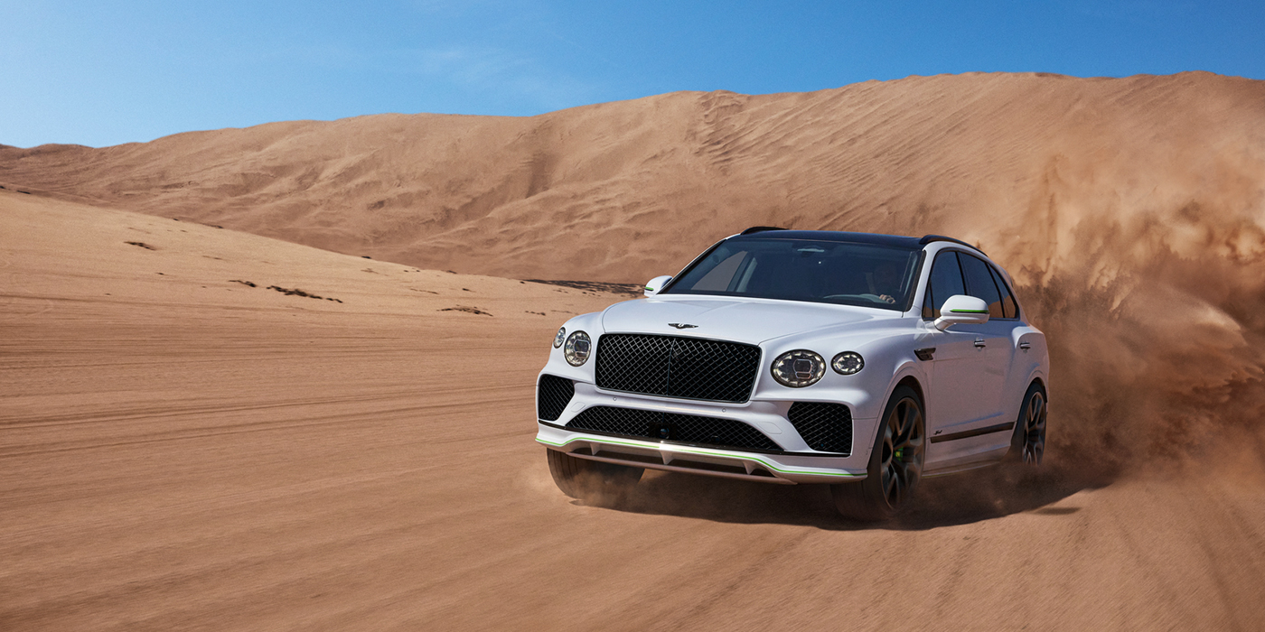 Bentley Paris Seine Bentley Bentayga Speed SUV front three quarter in Snow Quarts Pearlescent by Mulliner white paint driving dynamically through the desert