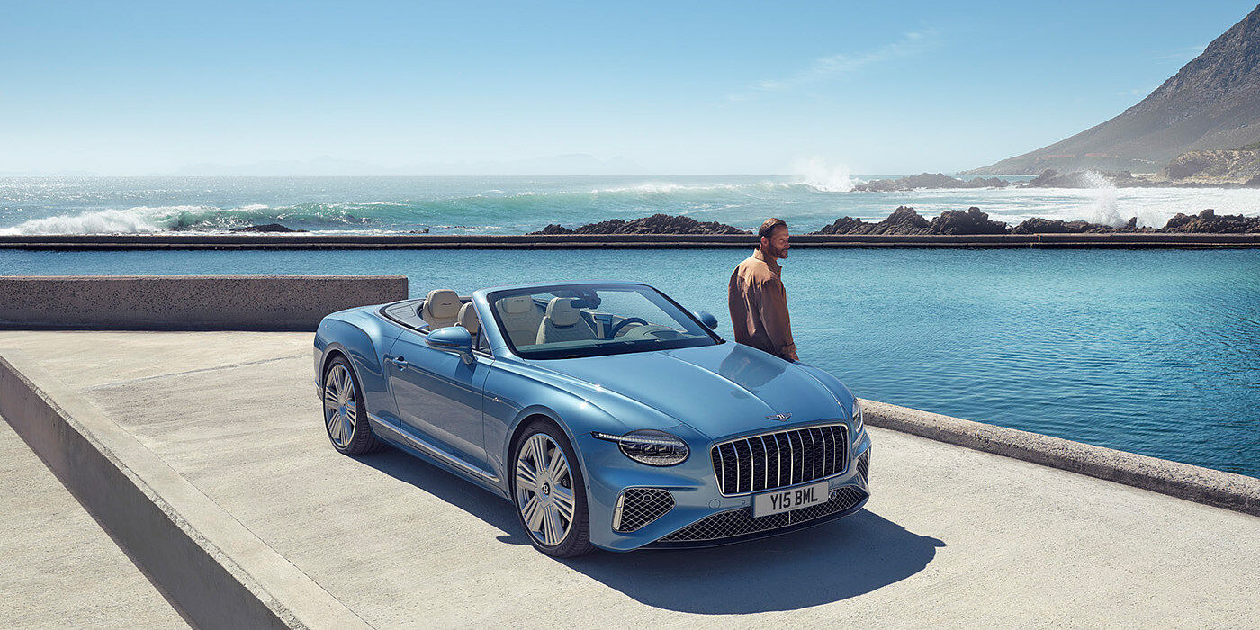 Bentley Paris Seine New Bentley Continental GTC Azure convertible front view in Light Windsor blue paint with 22 inch ten spoke wheels parked by the sea in the sunshine