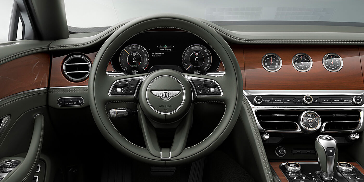 Bentley Paris Seine New Bentley Flying Spur sedan front cabin in Cumbrian Green hide and Crown Cut walnut veneer showing steering wheel and Rotating Display with three clocks on face