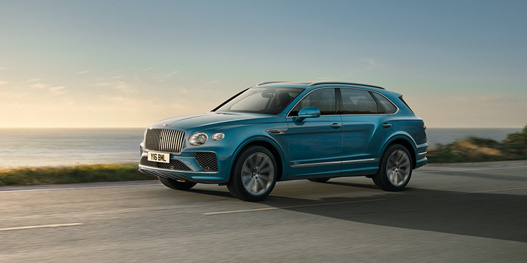 Bentley Paris Seine Bentley Bentayga Azure SUV in Topaz blue paint driving dynamically by the ocean with 22 inch 10 spoke directional wheels