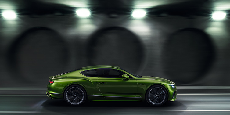 Bentley Paris Seine Bentley Continental GT Speed coupe profile in Tourmaline Green driving dynamically past a concrete wall at night