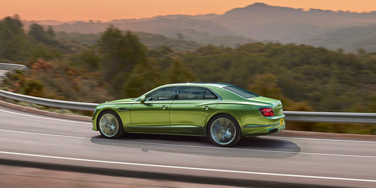 Bentley Paris Seine Bentley Flying Spur Speed sedan side profile in Tourmaline Green paint driving dynamically on a mountain road at sunset