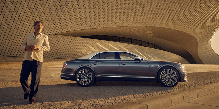 Bentley Paris Seine Bentley Flying Spur Mulliner sedan in Rose Gold over Magnetic duotone paint parked by a curved wall with person in suit jacket standing on the left