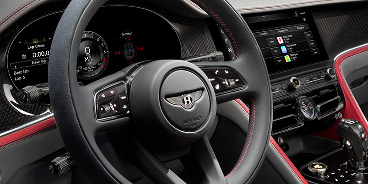 Bentley Paris Seine Bentley Flying Spur Speed sedan front interior detail showing steering wheel and driver screens surrounded with Hotspur red and Gravity Grey hides